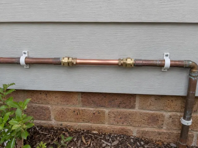 Repaired copper water pipe on an exterior wall above a brick base in Ashtonfield